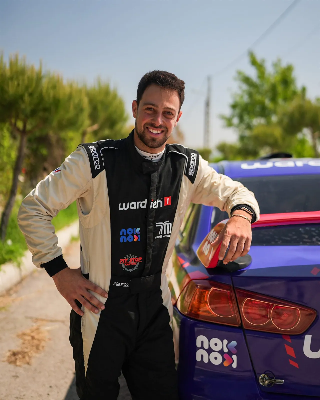 Carl Rizk in his race suit beside the rally car